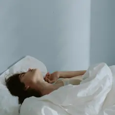 Kobieta leży w pościeli, z głową odrzuconą do tyłu. Wygląda jakby walczyła ze zmorą nocną, próbując złapać oddech.